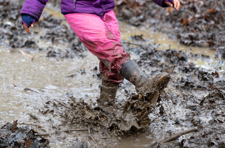 A child having fun at Mudfest, playfully kicking up squishy mud